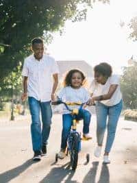 Child riding a bike with parents helping.